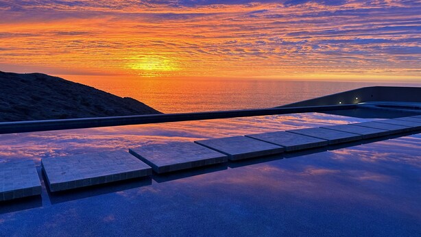 Ein Sonnenuntergangsblick von einem Balkon mit einem spiegelnden Pool und einem Steinweg.
