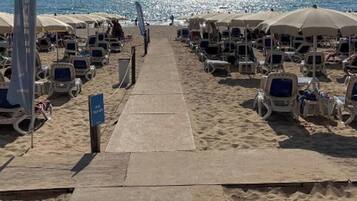 Une plage bordée de rangées de chaises longues et de parasols, une promenade en béton et une vue dégagée sur la mer.