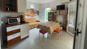 A compact kitchen with a microwave, a dining table with chairs, a sofa, and a TV on a shelf. - Holiday Home "Kastalia - La Relax" with Sea View, Shared Pool and Wi-Fi (Ragusa)