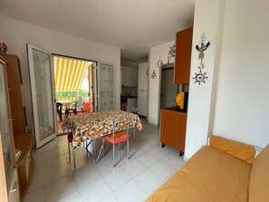 En kompakt opholdsstue med spisebord, sofa, tekøkken og en skydedør til et udendørs område.