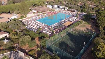 Vue aérienne d’un complexe hôtelier doté d’une piscine, de chaises longues et d’un court de tennis.