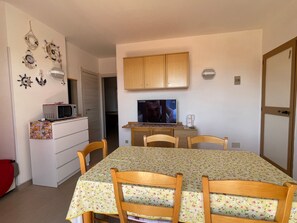 A dining area with a table set for four, a microwave, a television, and wooden cabinets above the table.