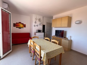 A compact living space with a dining table, chairs, a red sofa, a TV, and a microwave.