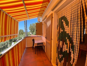 A balcony with a striped awning, a table with chairs, and a patterned door.