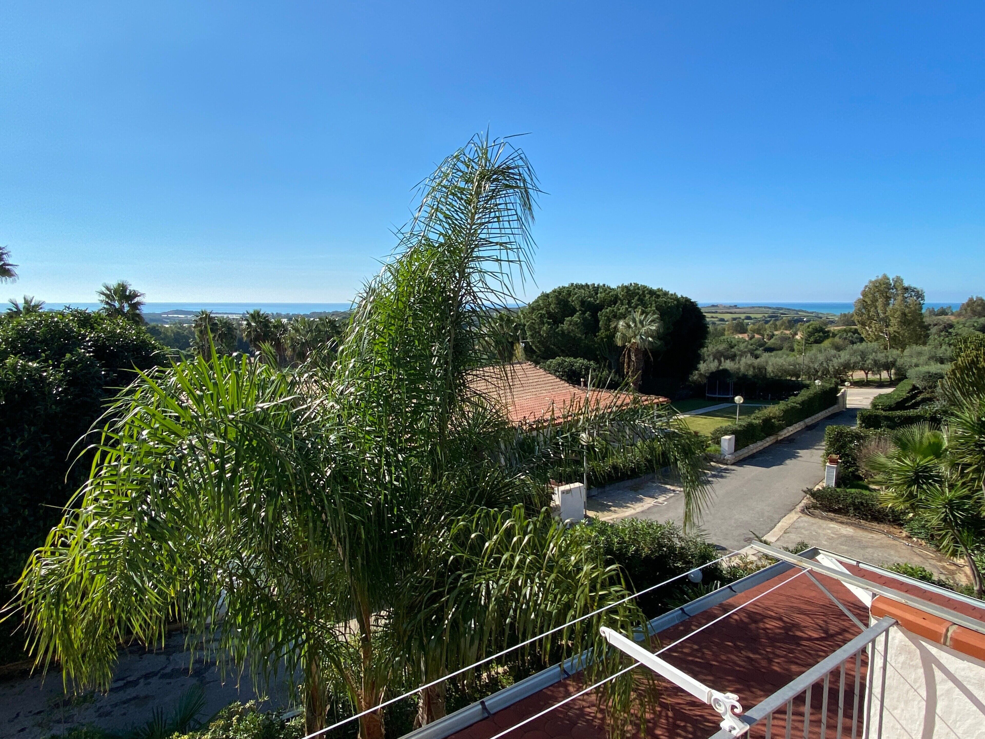 Un quartier résidentiel caractérisé par des toits recouverts de tuiles rouges, une végétation luxuriante et une vue dégagée sur la mer.
