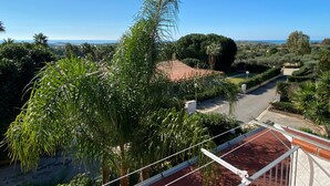 Un quartier résidentiel caractérisé par des toits recouverts de tuiles rouges, une végétation luxuriante et une vue dégagée sur la mer.