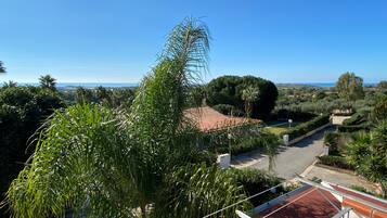 Un quartier résidentiel caractérisé par des toits recouverts de tuiles rouges, une végétation luxuriante et une vue dégagée sur la mer.