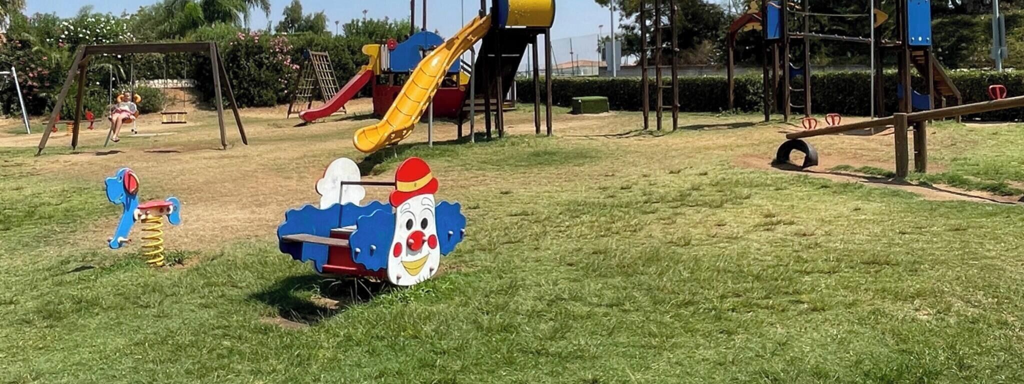 Un parque infantil con un tobogán, columpios y un pequeño coche de juguete azul y rojo.
