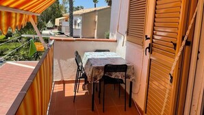 Un balcon avec une table et des chaises, une porte en bois et un sol carrelé.