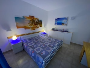 A bedroom with a bed, nightstands, a desk, and a painting of a sunset. - Holiday Home "Kastalia - Blu" with Sea View, Shared Pool and Wi-Fi (Ragusa)