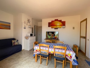 A dining area with a table set for four, a microwave, and a television on a stand. - Holiday Home "Kastalia - Blu" with Sea View, Shared Pool and Wi-Fi (Ragusa)