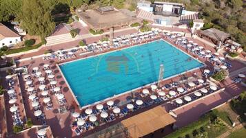 Vue aérienne d’un complexe hôtelier doté d’une grande piscine, entourée de transats et de parasols.