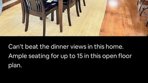 A spacious dining area with ample seating for up to 15 people, featuring a large table and chairs, a fireplace, and a view of the outdoors.