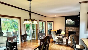A spacious dining area with a large wooden table and chairs, a fireplace, and a view of the outdoors.