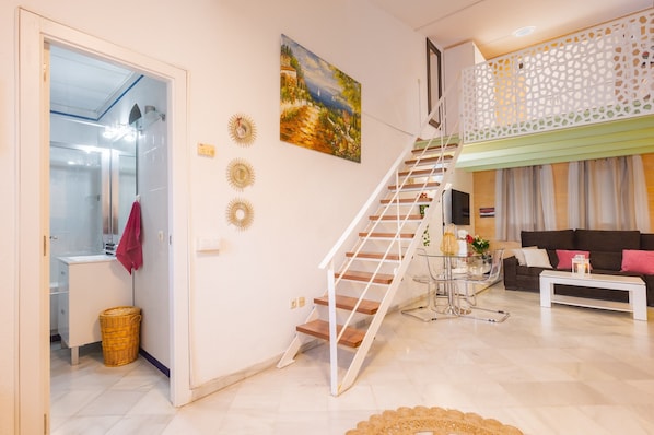 A modern living room with a staircase, a sofa, a coffee table, and a painting on the wall.