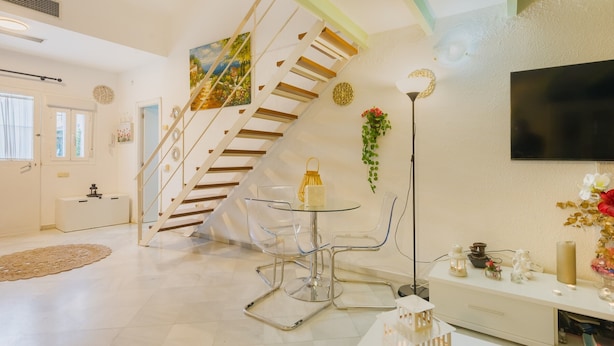 A modern living room with a staircase, a round glass table, and a flat-screen TV. - Exclusive Duplex Penthouse with Private Terrace in the Heart of Seville (Sevilla)