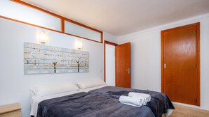Une chambre avec deux lits, une armoire en bois, une œuvre d’art accrochée au mur et une table de chevet.