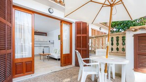 Une terrasse ouverte avec une table et des chaises, une porte en bois et une vue sur une pièce qui comprend une cuisine.