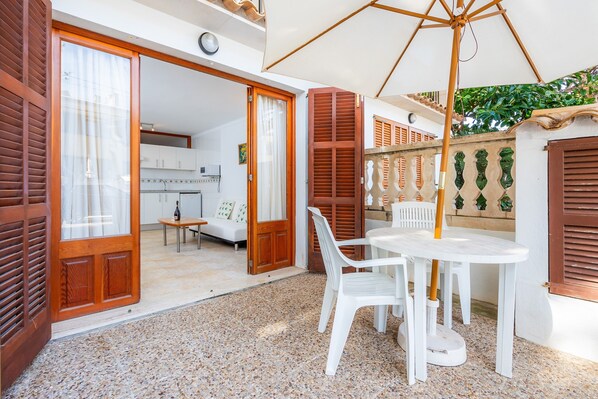 An open patio with a table and chairs, a wooden door, and a view into a room with a kitchen.