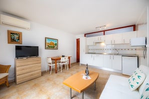 A compact living space with a kitchenette, a dining area, a sofa, and a TV.