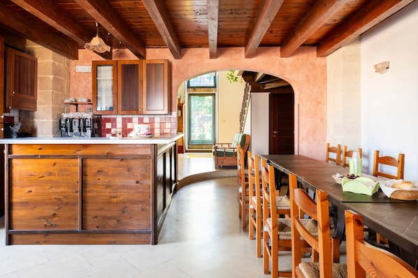 Une cuisine rustique avec des meubles en bois, un îlot central et un coin repas comprenant des chaises en bois et une longue table.
