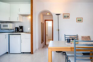 Una cocina compacta con armarios blancos, microondas, cafetera y refrigerador.
