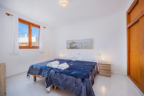 Un dormitorio con cama, dos mesitas de noche, un armario ropero de madera y una ventana con cortinas, además de un cuadro en la pared.
