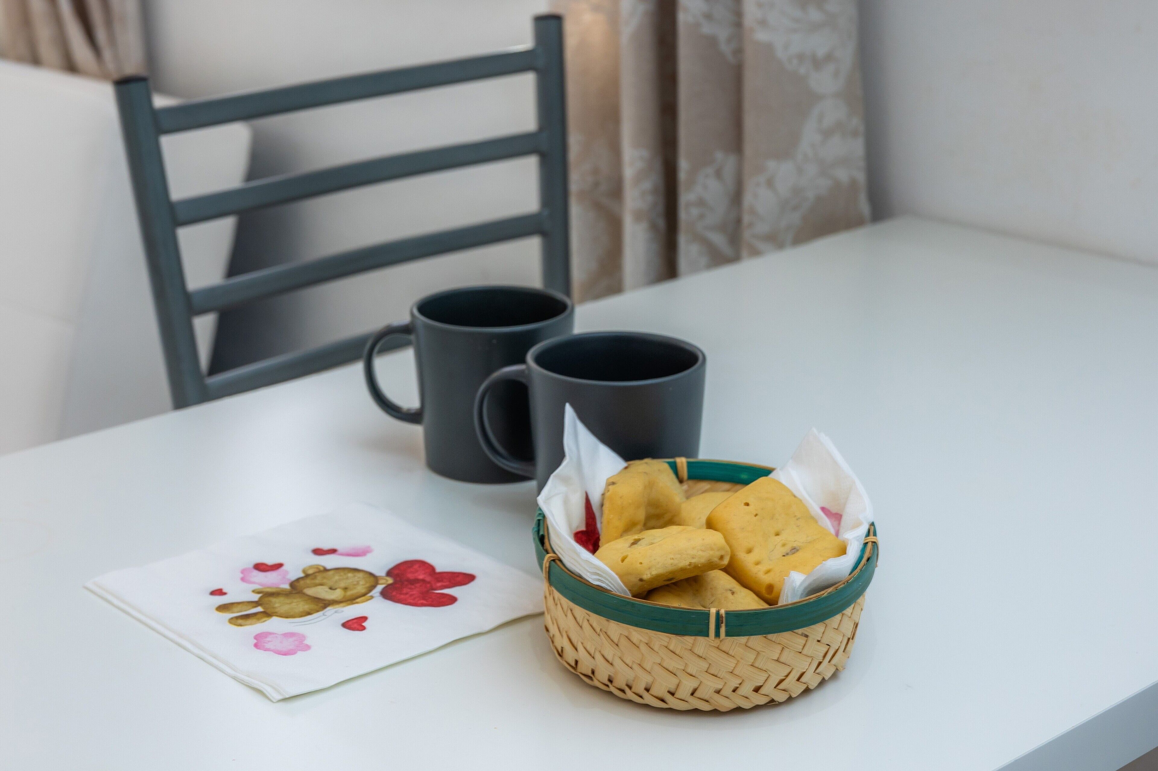 A table with a basket of cookies and two black mugs.