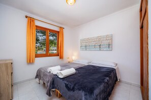 Une chambre avec deux lits, une fenêtre avec des rideaux, un tableau au mur et une armoire en bois.
