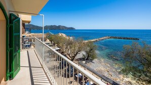 A balcony with a view of the sea, a rocky shoreline, and a distant mountain.