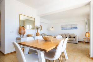 A modern dining area with a wooden table, white chairs, a large mirror, and a sofa in the background. - Holiday Apartment "Duplex Voramar Mhm Seafront" with Sea View, Balcony & Wi-Fi (Cala Bona)