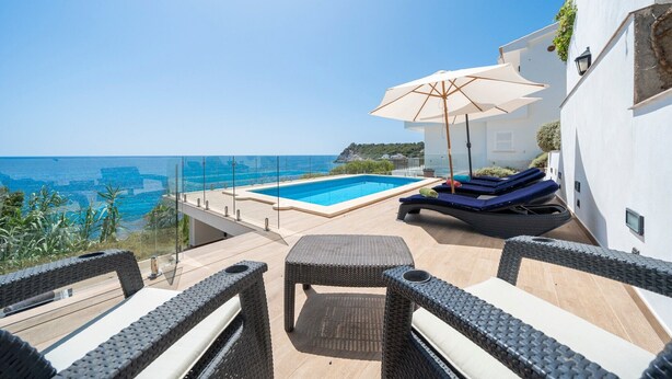 A rooftop pool with a clear view of the sea, a lounge area with a table and chairs, and a large umbrella.