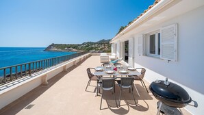 A terrace with a table set for dining, a grill, and a view of the sea.