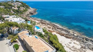 A coastal property with a swimming pool, rocky beach, and a view of the sea.