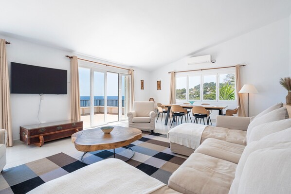 A modern living room with a sofa, a coffee table, a TV, and a dining area with chairs and a table.
