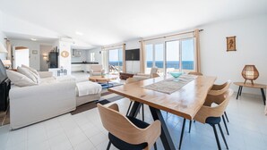 A modern living room with a dining area, a kitchen, and a balcony with a view of the sea.
