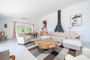 Een woonkamer met een bank, een salontafel, een eethoek met stoelen, een open haard en kunstwerken aan de muren.