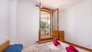 Une chambre à coucher avec un lit, une commode en bois et une salle de bain visible à travers une porte ouverte.