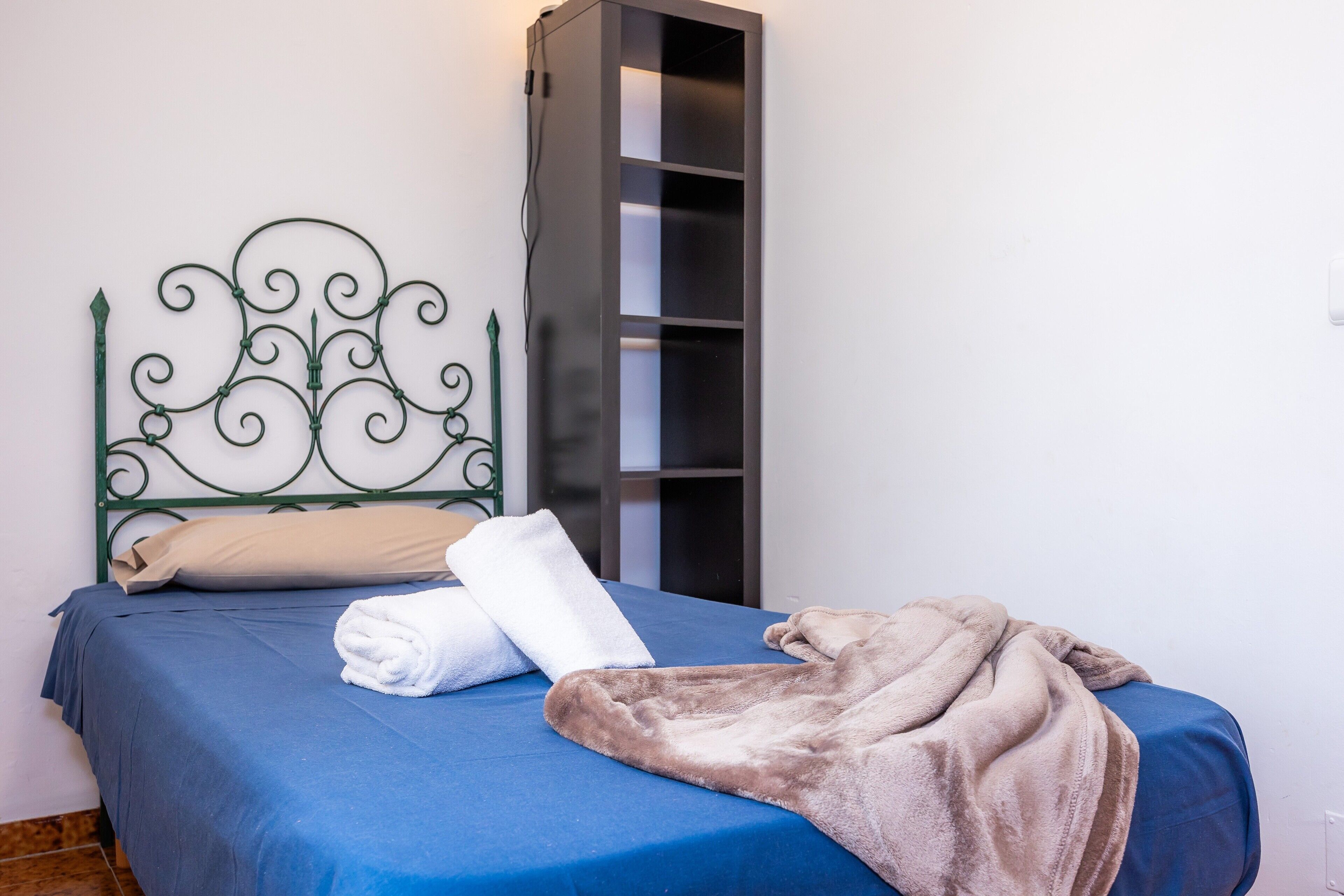 A bed with a blue bedspread, a white pillow, and a folded white towel.