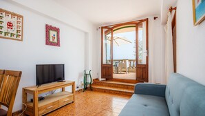 Un salon avec un téléviseur, des meubles en bois, un canapé bleu et une vue sur l’extérieur par une porte ouverte.