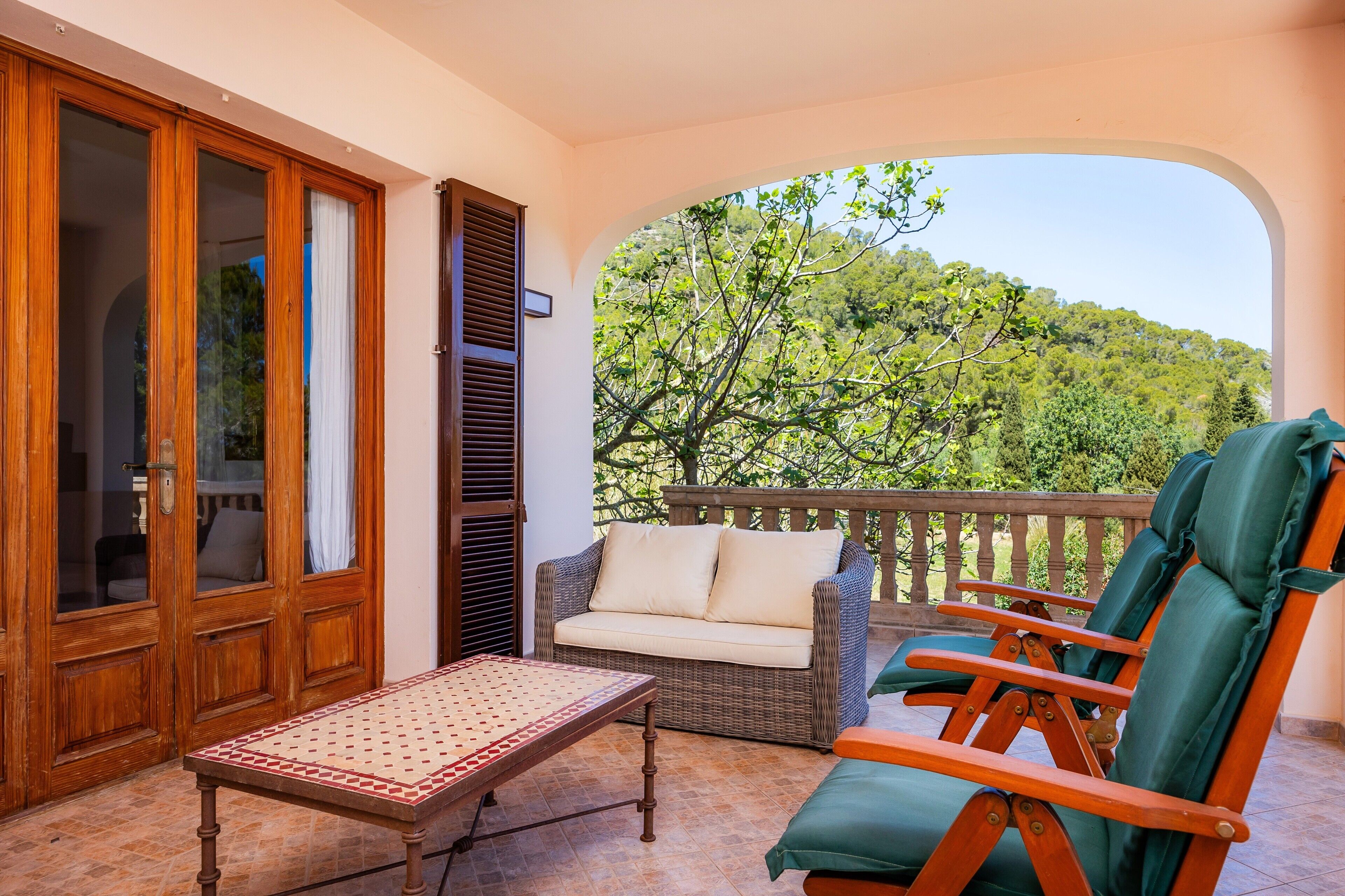 A balcony with wicker furniture, a table, and a view of a forested hillside.