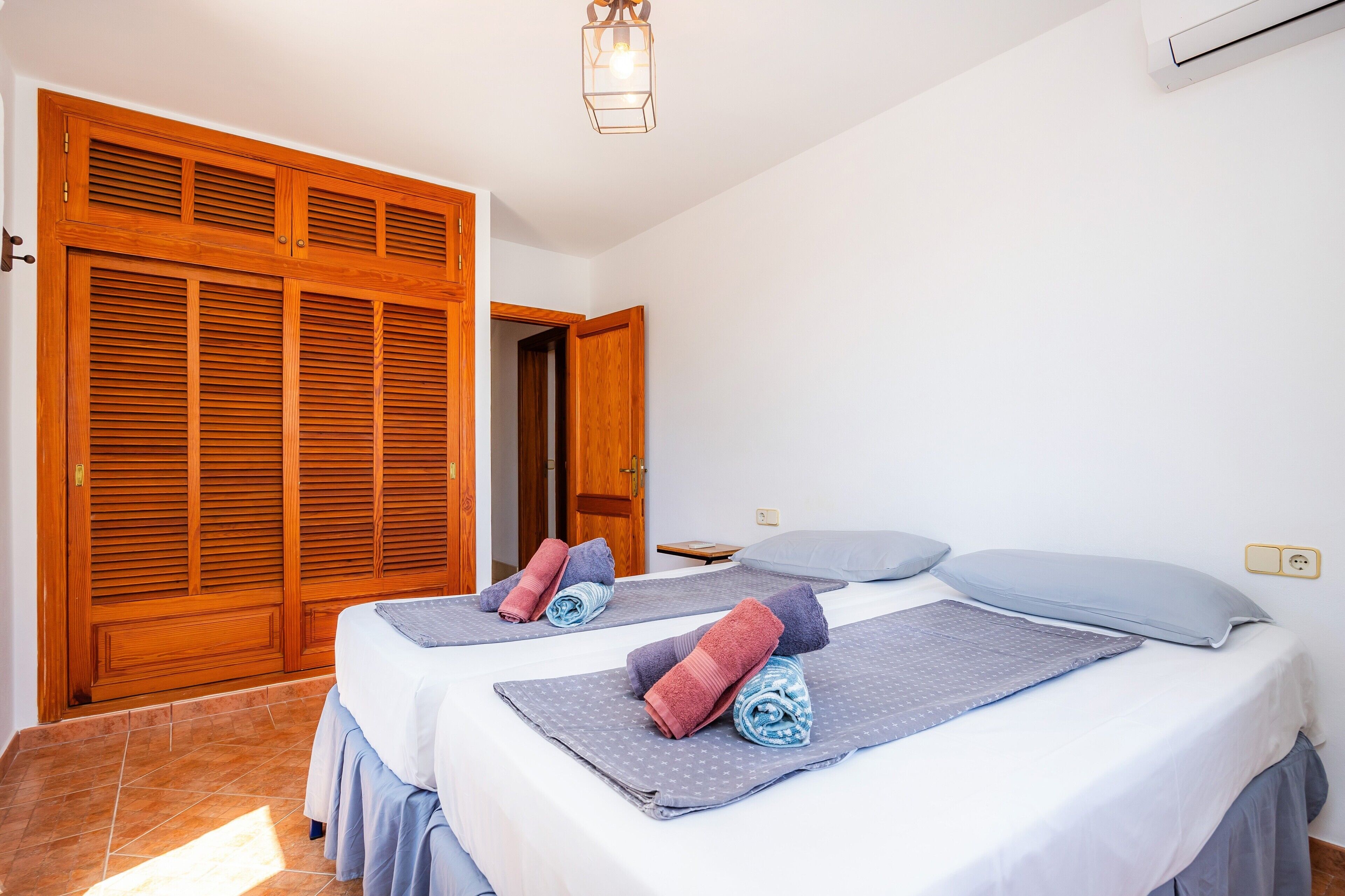 Een hotelkamer met twee bedden, houten kasten, een plafondlamp en een stopcontact aan de muur.