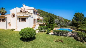Eine weiße Villa mit Swimmingpool, umgeben von viel Grün und Hügeln.