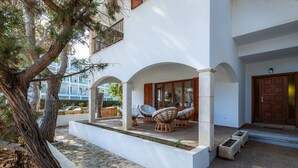 A modern building with a white facade, outdoor seating area with wicker chairs, and a large tree in the foreground. - Vacation Home "Family Home Mhm" near Beach with Private Terrace & Wi-Fi (Cala lliteres)