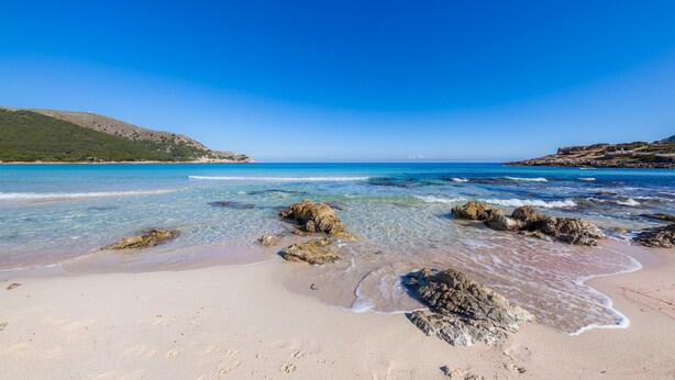 A beach with clear water, rocks, and a distant hill. - Vacation Home "Family Home Mhm" near Beach with Private Terrace & Wi-Fi (Cala lliteres)