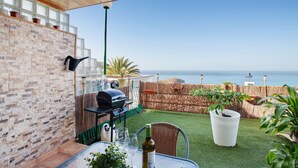 A patio with a grill, a table with glasses, and a view of the sea. - Vacation Home "Sunset" with Sea View, Shared Pool & Wi-Fi (Puerto Rico)