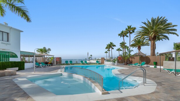 A swimming pool with lounge chairs, palm trees, and a view of the ocean. - Vacation Home "Sunset" with Sea View, Shared Pool & Wi-Fi (Puerto Rico)