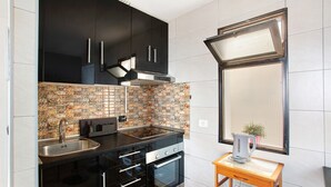A modern kitchen with black cabinets, a tiled backsplash, a stainless steel sink, and a kettle on a small wooden table. - Vacation Home "Sunset" with Sea View, Shared Pool & Wi-Fi (Puerto Rico)