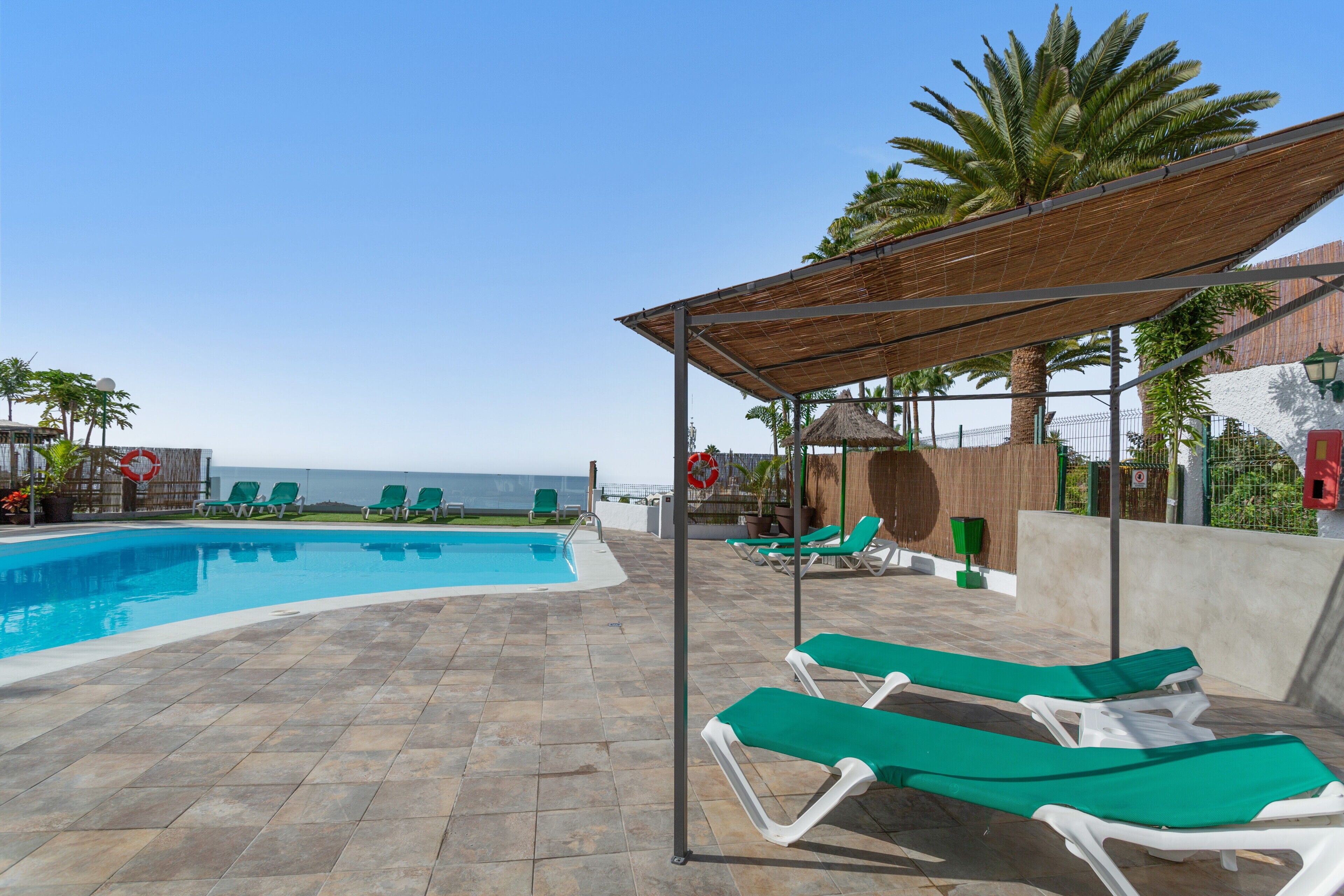 Zona de piscina con sillones de descanso, una pérgola y vistas al mar.