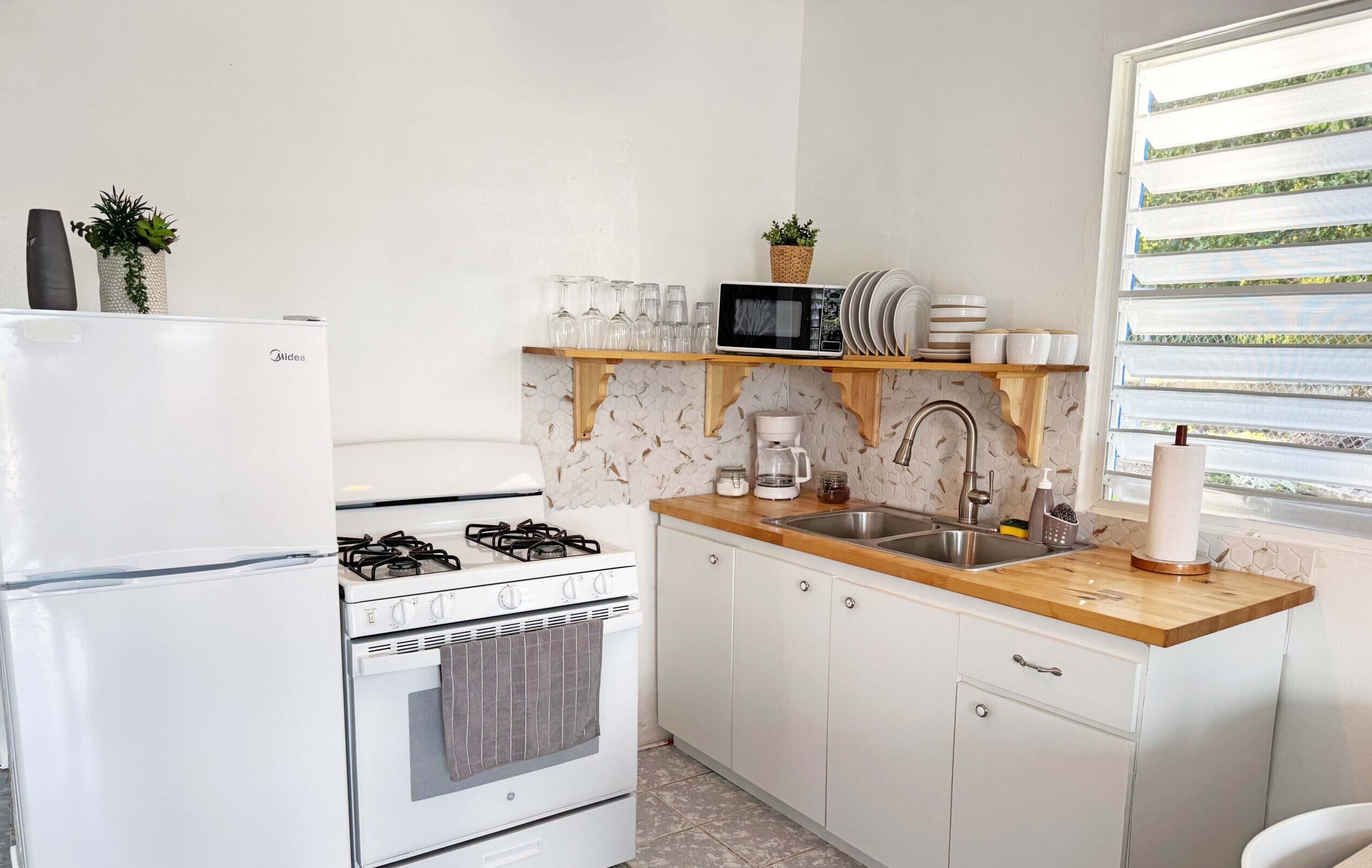 A compact kitchen with a refrigerator, stove, oven, microwave, and a wooden countertop.